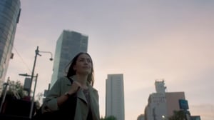 Mujer en primer plano con ciudad de fondo. Inicio del comercial titulado 