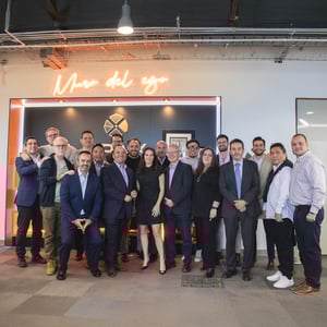 Grupo de personas posando en un espacio corporativo moderno con iluminación cálida y letrero de neón que dice 'Muro del ego', junto a un panel decorativo con logotipo.