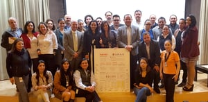 Grupo de personas reunidas en un auditorio, sosteniendo un cartel con el título ‘Plan 2017’ y el logotipo de UPAX, que muestra objetivos, estrategias y firmas.