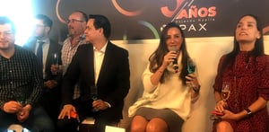 Celebración del aniversario de UPAX con personas sentadas sosteniendo copas, frente a un fondo decorado con el texto ‘5 años dejando huella’ y el logotipo de la empresa.